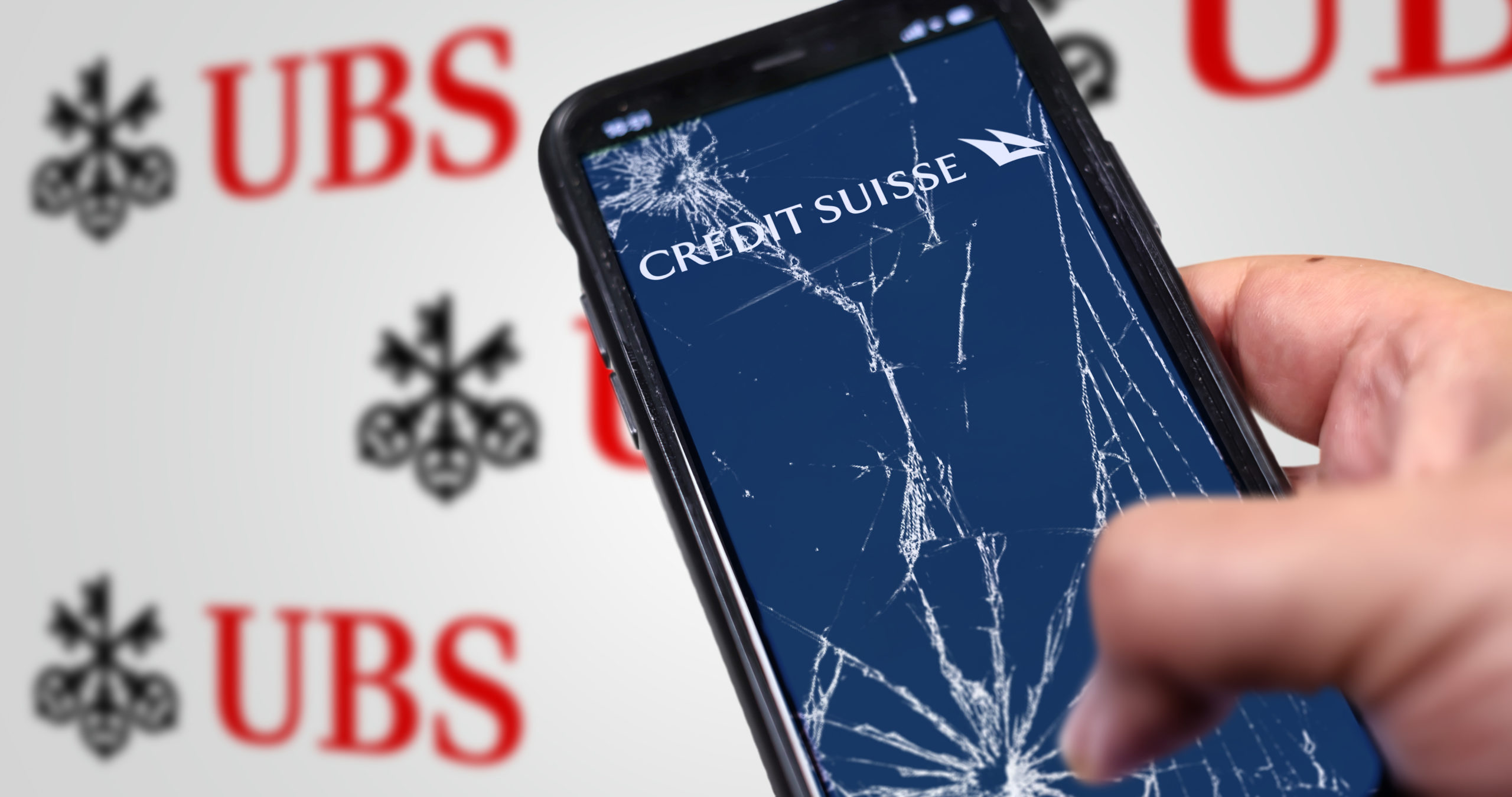Hand holding a phone with the Credit Suisse logo on the cracked screen